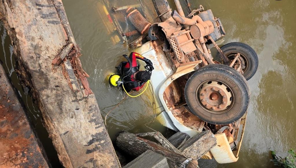 Bombeiros resgatam corpo de vítima presa às ferragens após caminhão tombar e cair em rio